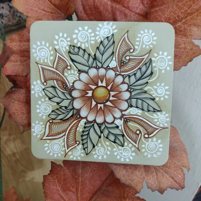 OMNU flower drawn on a tinted tile, surrounded by autumn leaves